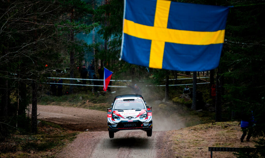 En rallybil flyger över en skog. (AI text)