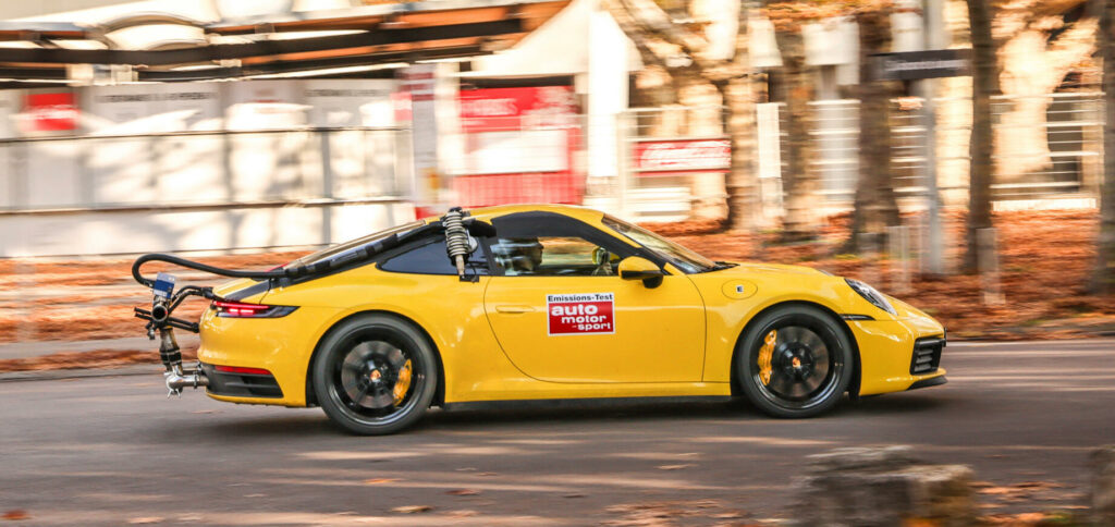 En gul Porsche 911 GTS kör nerför en gata. (AI text)