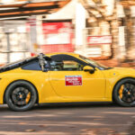 En gul Porsche 911 GTS kör nerför en gata. (AI text)