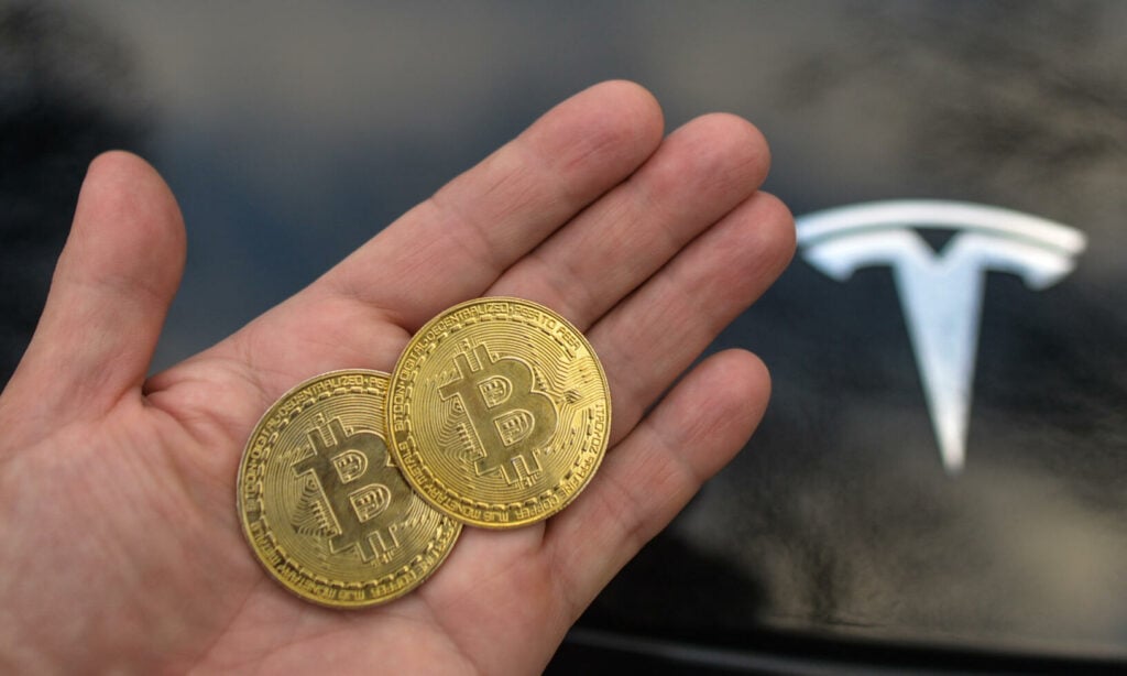 En person håller två bitcoine framför en Tesla. (AI text)