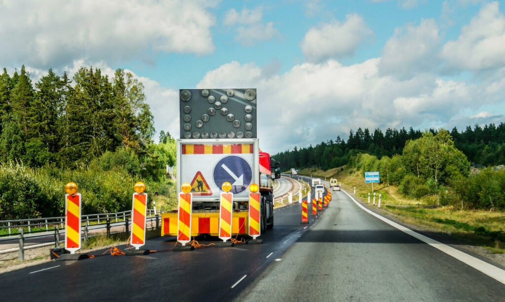 En väg med byggarbetsplatser och spärrar samt en skylt. (AI text)