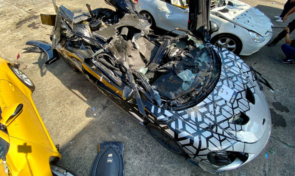 En grupp personer står sammanlagt kring en bil. (AI text)