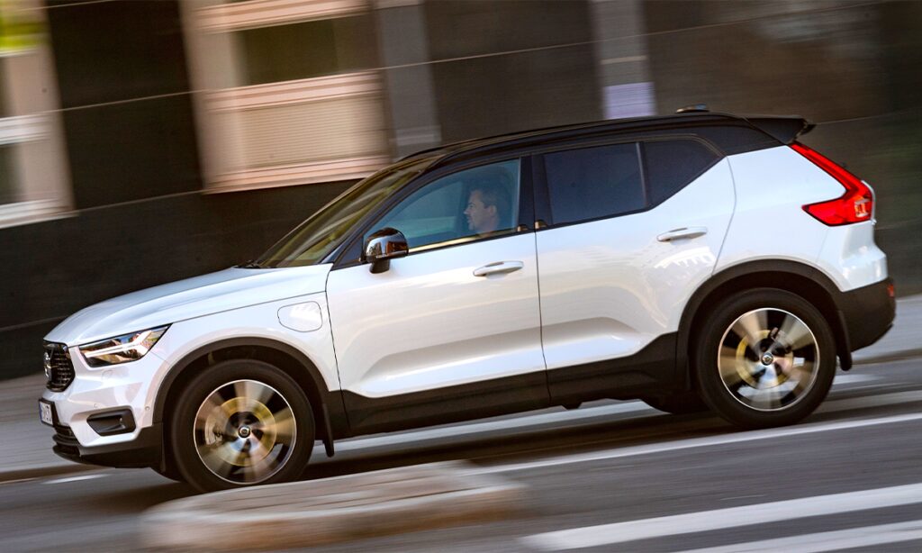 En vit Volvo XC90 SUV kör nedför en stadsgata. (AI text)