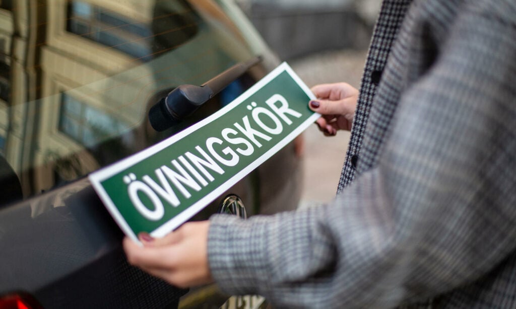 En man sätter upp en skylt på bakdelen av en bil. (AI text)