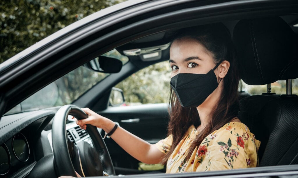 En kvinna som bär ansiktsmask kör bil. (AI text)