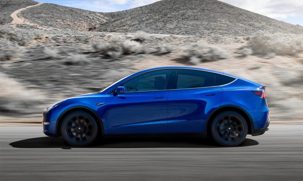 En blå Tesla Model Y kör nedför en bergväg. (AI text)