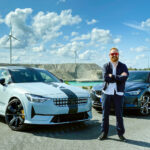 En man står bredvid en bil och vindkraftverk. (AI text)