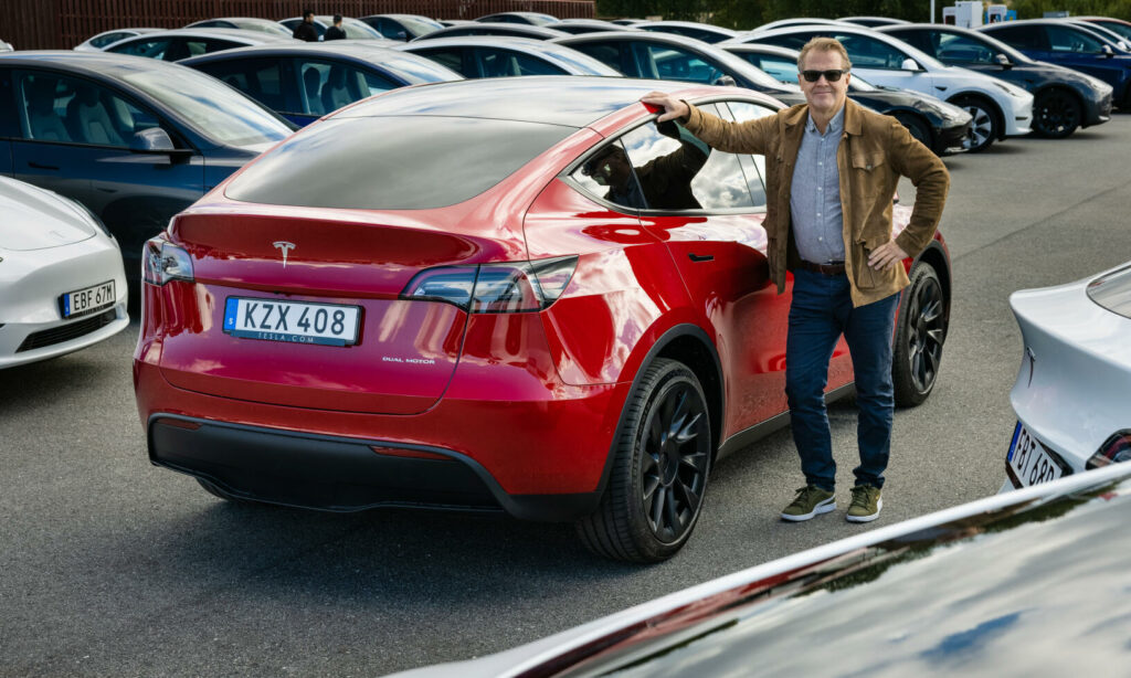 En man står bredvid en Tesla Model S i en parkeringsplats. (AI text)
