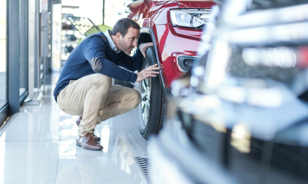 En man knäler ner för att inspektera en bil i en showrum. (AI text)