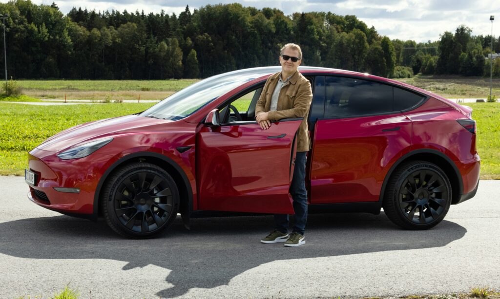 En man står bredvid en röd Tesla Model Y. (AI text)