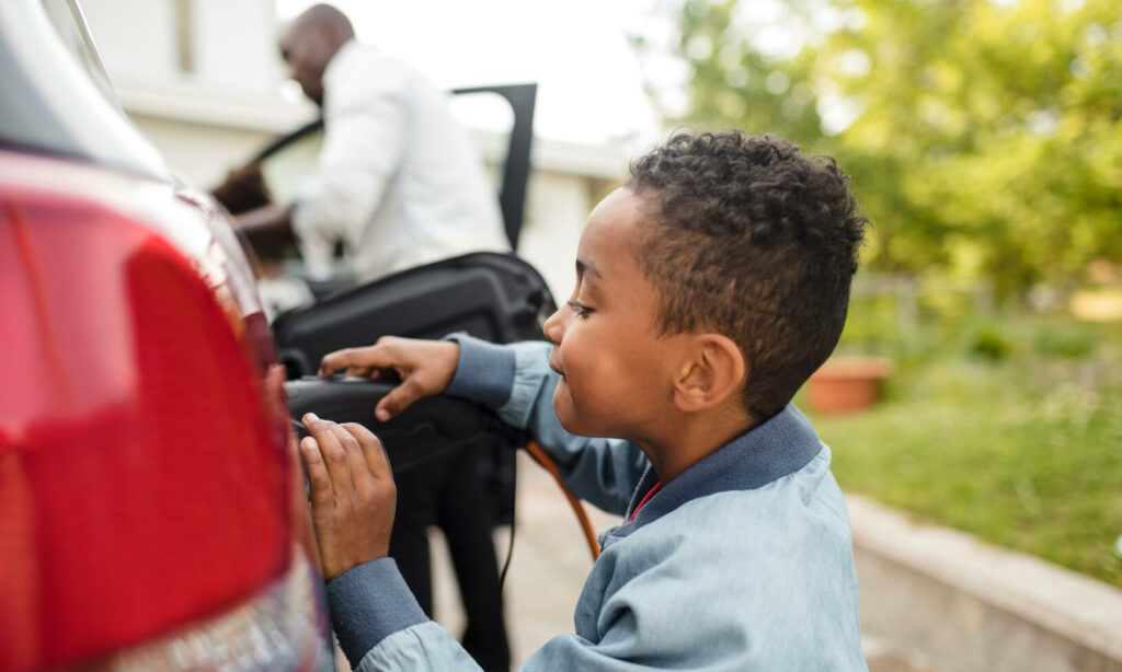 En ung pojke sätter in en bilbatteriladdare i hans bil. (AI text)