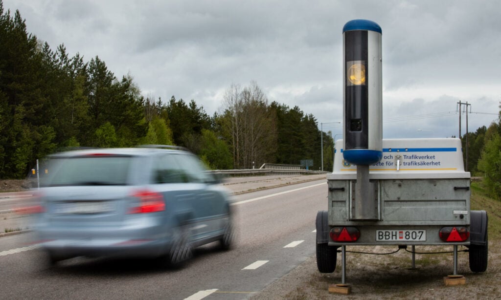 En bil kör nedför en väg med ett släp fäst bakom den. (AI text)