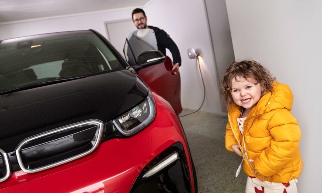 En familj står bredvid en BMW i3 elbil. (AI text)