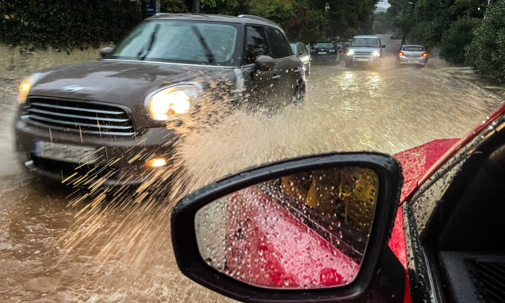 En bil kör genom en översvämmad gata. (AI text)