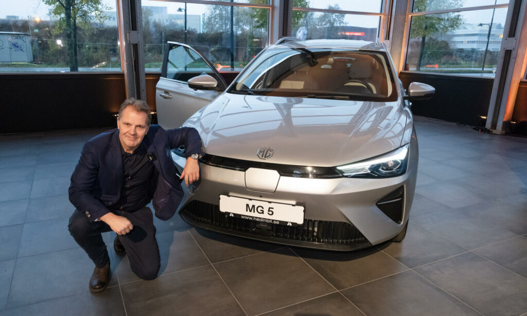 En man knäböjer bredvid en bil. (AI text)