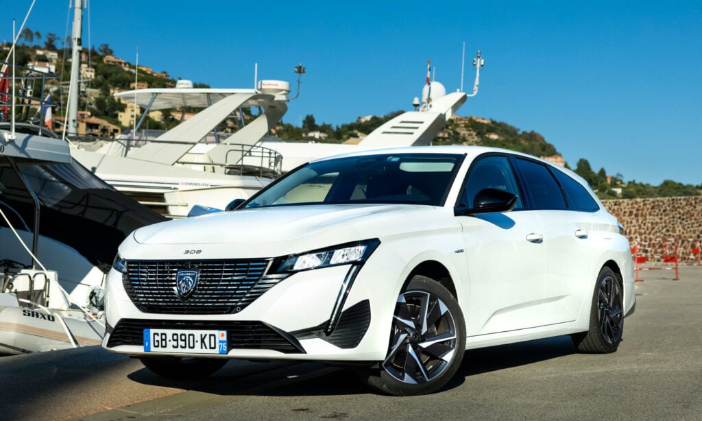 En vit bil parkerad på en piersida bredvid en yacht. (AI text)