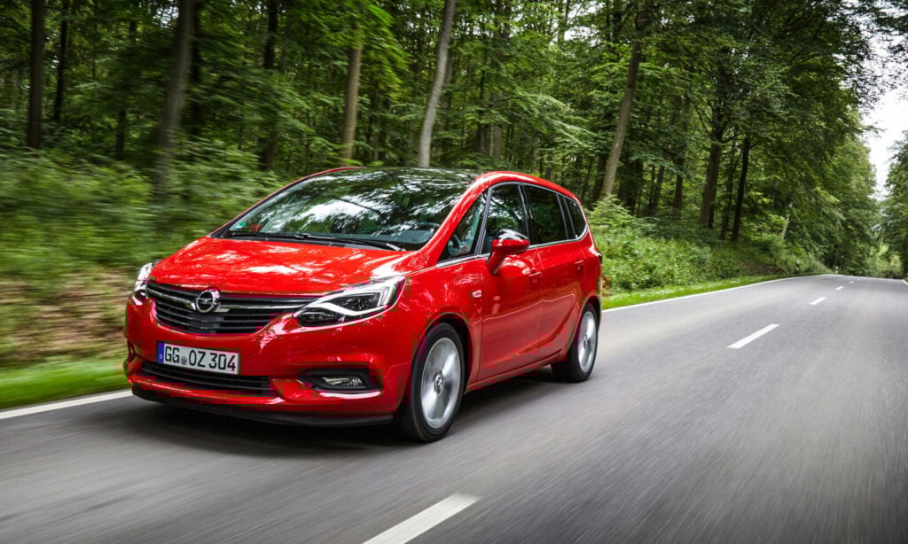 En röd Opel Zafira kör längs en landsväg. (AI text)