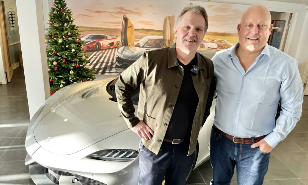 Två män står bredvid en bil. (AI text)