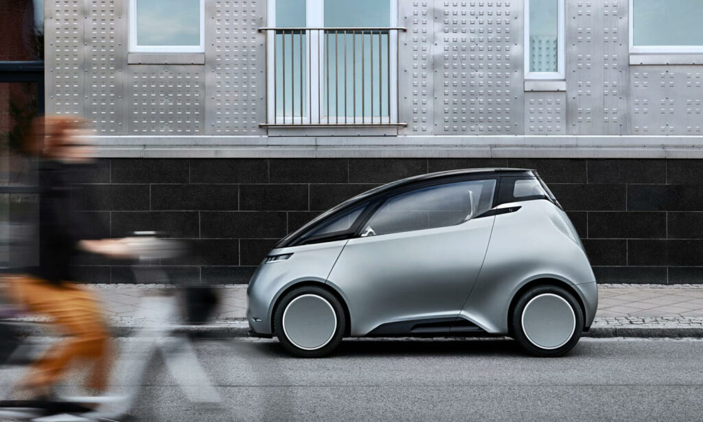 En kvinna cyklar bredvid en futuristisk bil. (AI text)