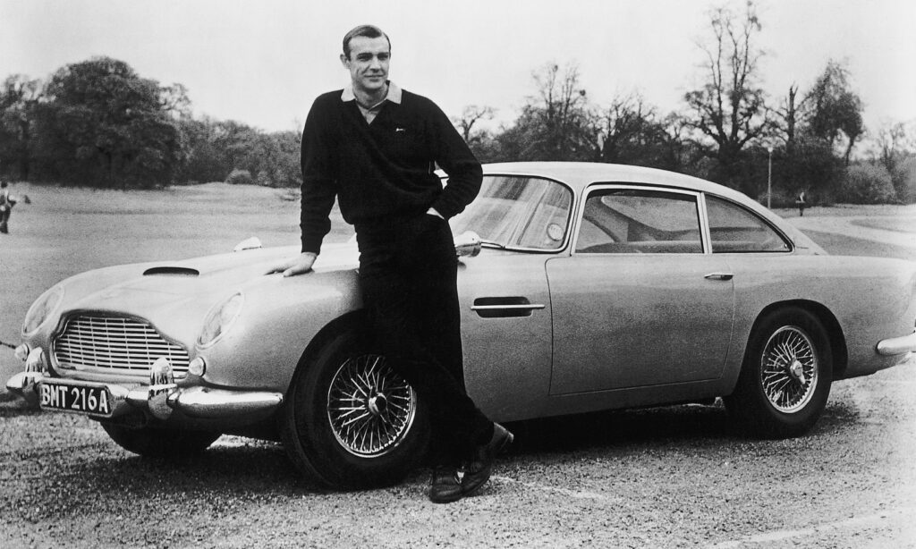 Sean Connery som James Bond i Goldfinger (1964) med en av de fyra 1964 Aston Martin DB5:orna som användes i produktionen.