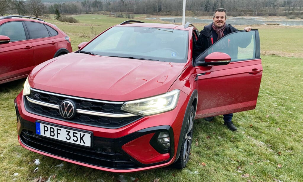 En man står bredvid en röd Volkswagen T-Roc SUV. (AI text)