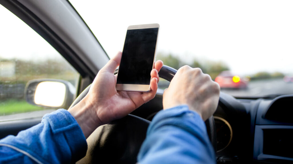 En man kör en bil samtidigt som han använder sin telefon. (AI text)