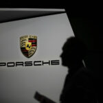 En man promenerar förbi en Porsche-logotyp på bilutställningen i Shanghai. Bild: Reuters. (AI text)