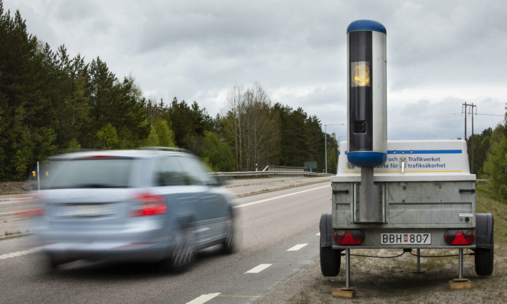 En bil kör nedför en väg med en släp upphängd bakom den. (AI text)