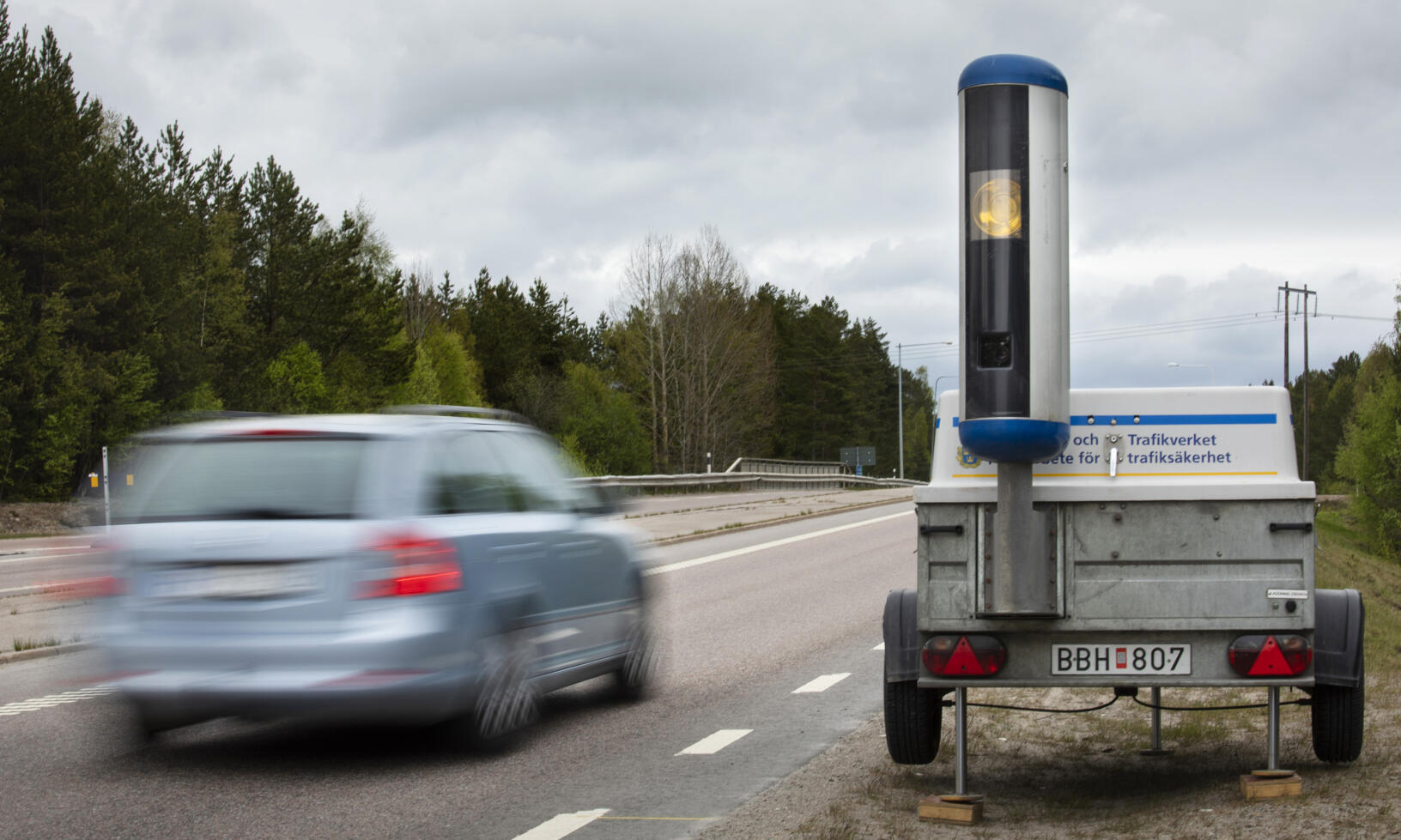 En bil kör nedför en väg med en släp upphängd bakom den. (AI text)