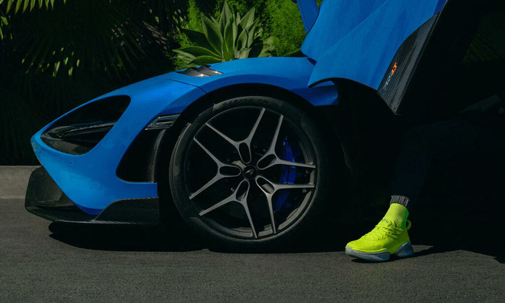 En man sittande på huven på en blå McLaren 720S. (AI text)