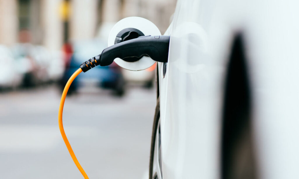 En vit bil är uppkopplad till en elladdare. (AI text)