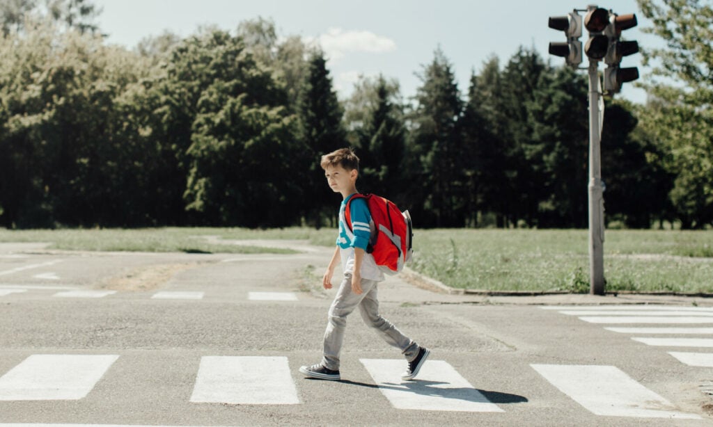 En pojke korsar gatan med ett ryggsäck. (AI text)