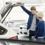 En bilförare och en passagerare undersöker en bil i en försäljningsanläggning. (AI text)