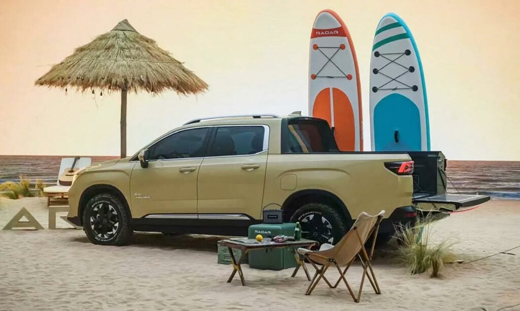 En Chevrolet-lastbil parkerad på stranden med surfbrädor och stolar. (AI text)