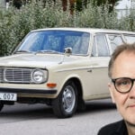 En man med glasögon står bredvid en bil. (AI text)
