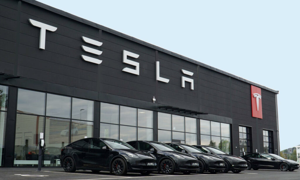 En Tesla-distributör med många bilar parkerade framför. (AI text)
