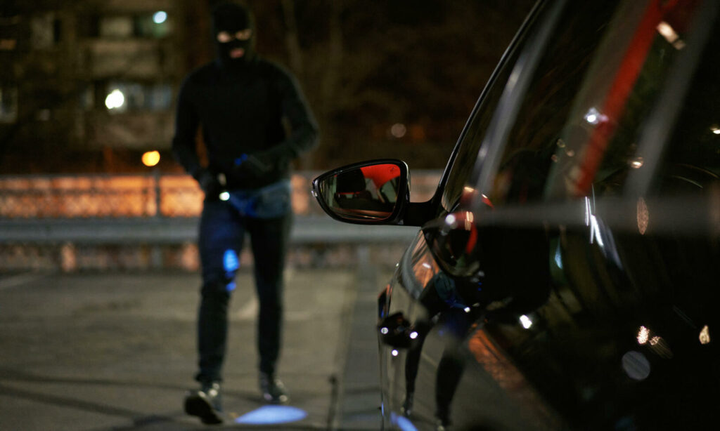 En man i svart mask går förbi en bil på natten. (AI text)