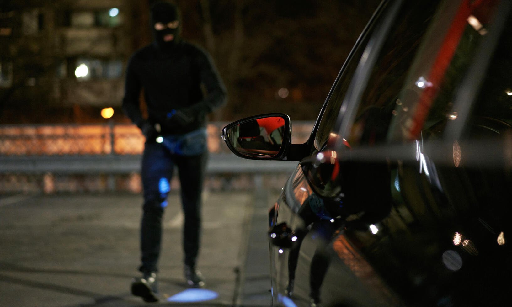 En man i svart mask går förbi en bil på natten. (AI text)