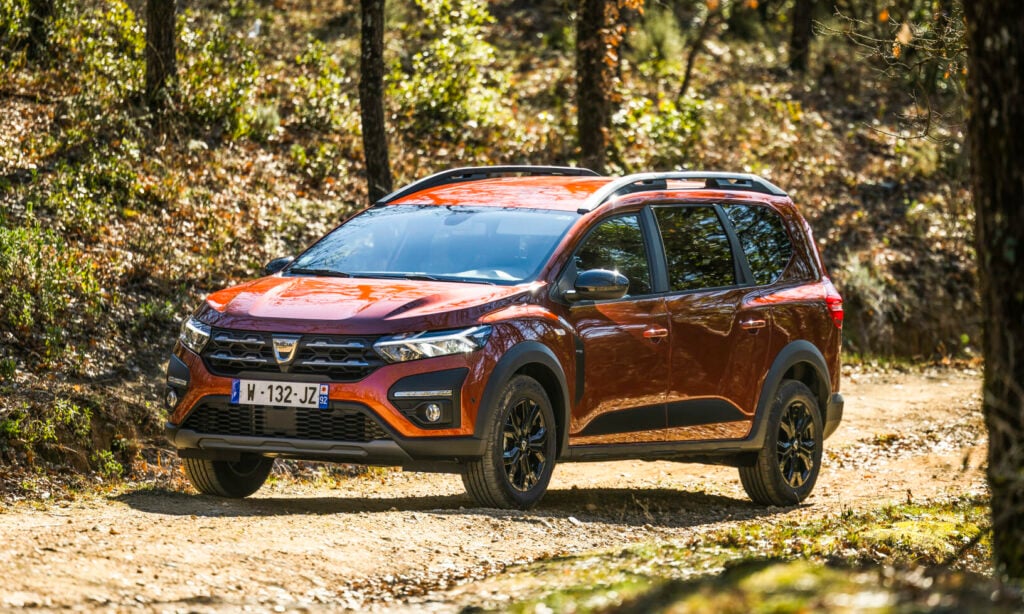 En röd bil kör längs en grusväg i skogen. (AI text)