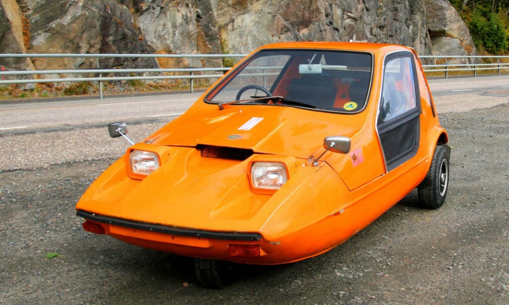 En liten orange bil står parkerad vid vägens kant. (AI text)