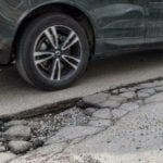 En bil står parkerad på en gata med en grop i vägen. (AI text)