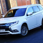 En vit bil står parkerad framför ett brutet hus. (AI text)