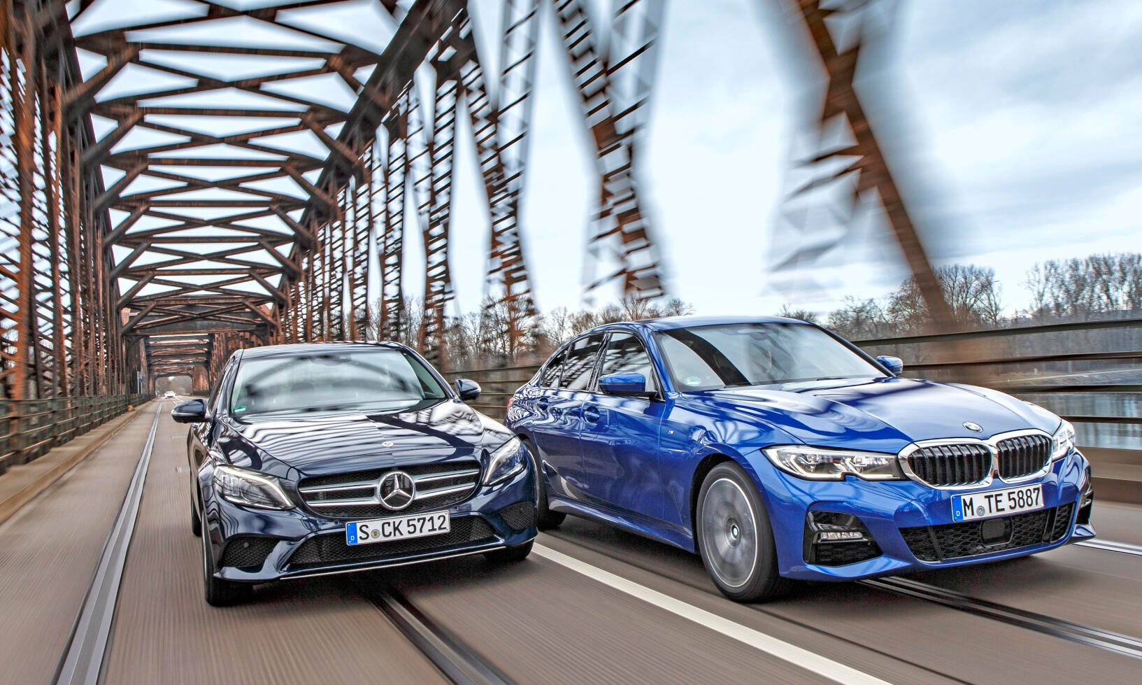 Två Mercedes-Benz E-klass-sedanter kör över en bro. (AI text)