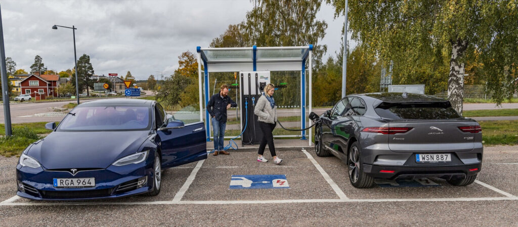 En Tesla Model S och en Tesla Model X parkerade vid en laddstation. (AI text)