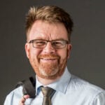 En man i kostym och slips poserar för en bild. (AI text)