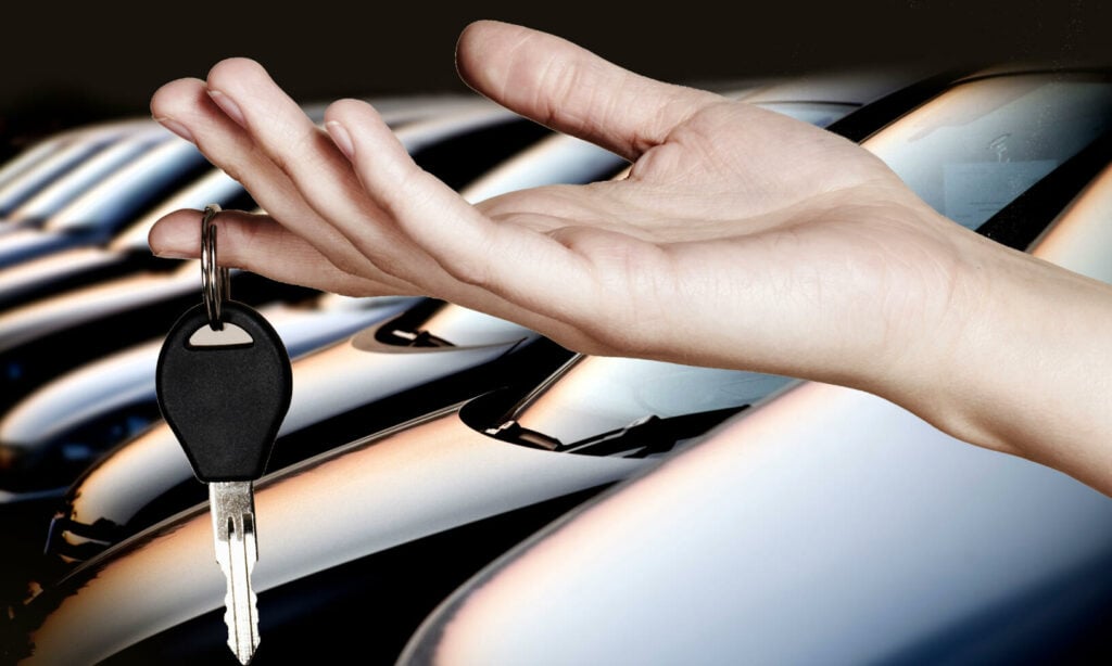 En person håller en bilnyckel framför en rad bilar. (AI text)