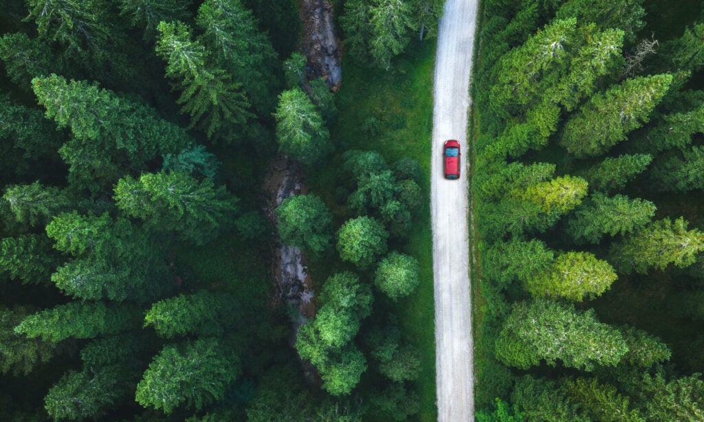 Utsikt från luften på en bil som kör genom ett skogsbryn. (AI text)