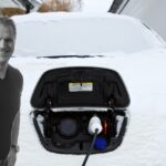 En man står bredvid en bil som är täckt av snö. (AI text)