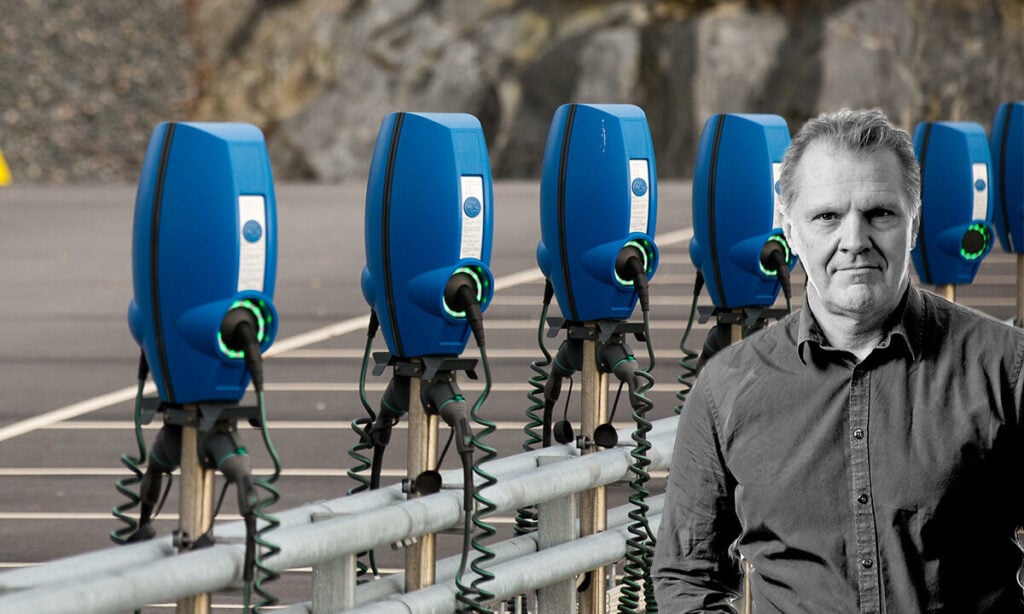 En man står bredvid en rad blå laddkontakter för elbilar. (AI text)