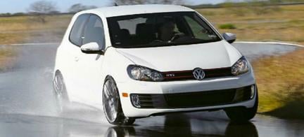 En vit Volkswagen Golf GTI kör på en våt väg. (AI text)
